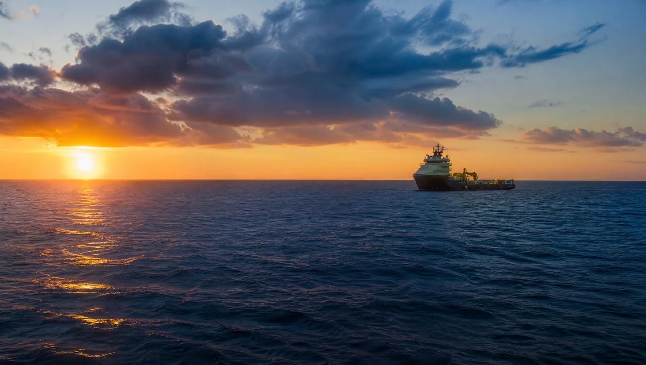 Survey vessel moving through open ocean during sunrise